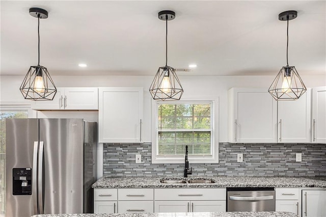 kitchen with backsplash, light stone counters, stainless steel appliances, white cabinetry, and a sink