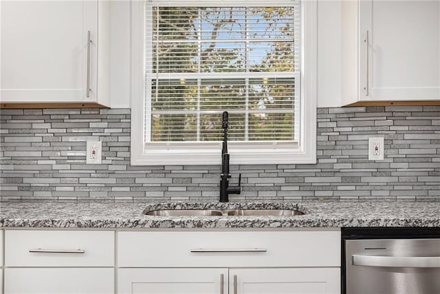 kitchen featuring stainless steel dishwasher, backsplash, white cabinetry, and a sink