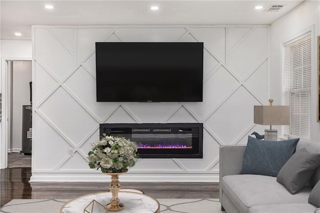 living area with visible vents, wood finished floors, a decorative wall, and a glass covered fireplace