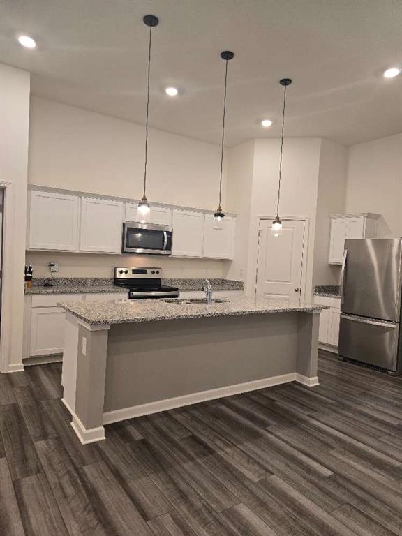 kitchen with pendant lighting, sink, white cabinets, stainless steel appliances, and a center island with sink