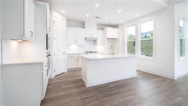 kitchen featuring a center island with sink, tasteful backsplash, hardwood / wood-style floors, and white cabinets