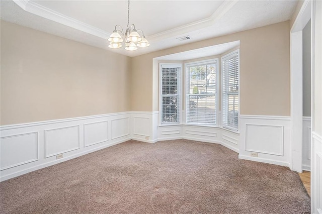 carpeted empty room featuring a raised ceiling, a chandelier, and ornamental molding