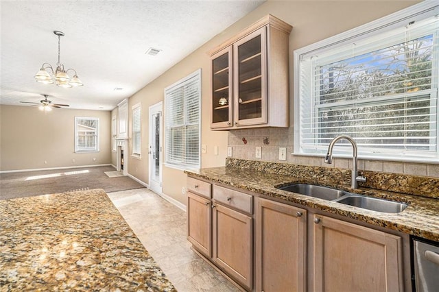 kitchen featuring stone counters, decorative backsplash, sink, hanging light fixtures, and ceiling fan with notable chandelier