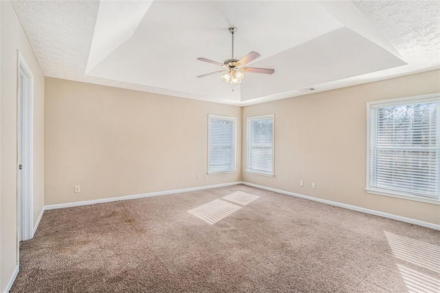 carpeted empty room with a textured ceiling, ceiling fan, and a raised ceiling