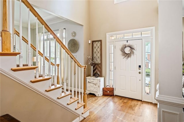 foyer featuring light wood finished floors, crown molding, and stairs