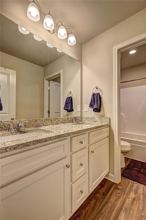 full bath featuring double vanity, a sink, toilet, and wood finished floors