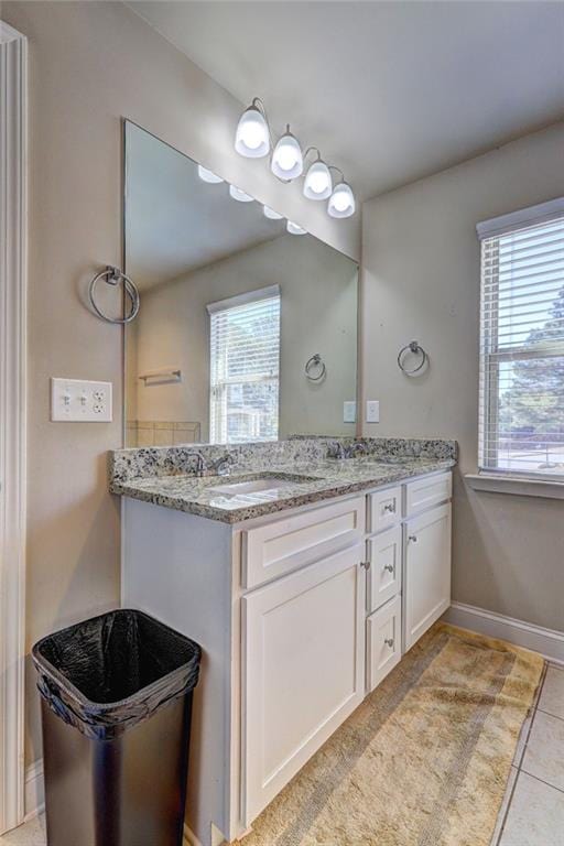 bathroom with baseboards, double vanity, a sink, and plenty of natural light