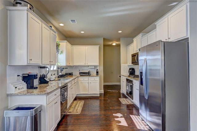 kitchen featuring dark wood-style flooring, light stone counters, white cabinetry, visible vents, and stainless steel appliances