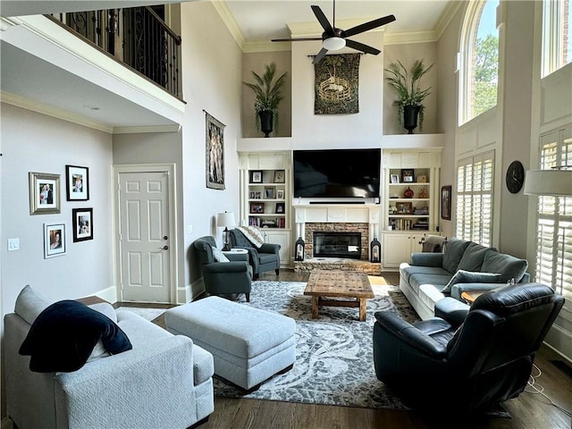 living area with a high ceiling, a fireplace, a ceiling fan, ornamental molding, and dark wood-style floors