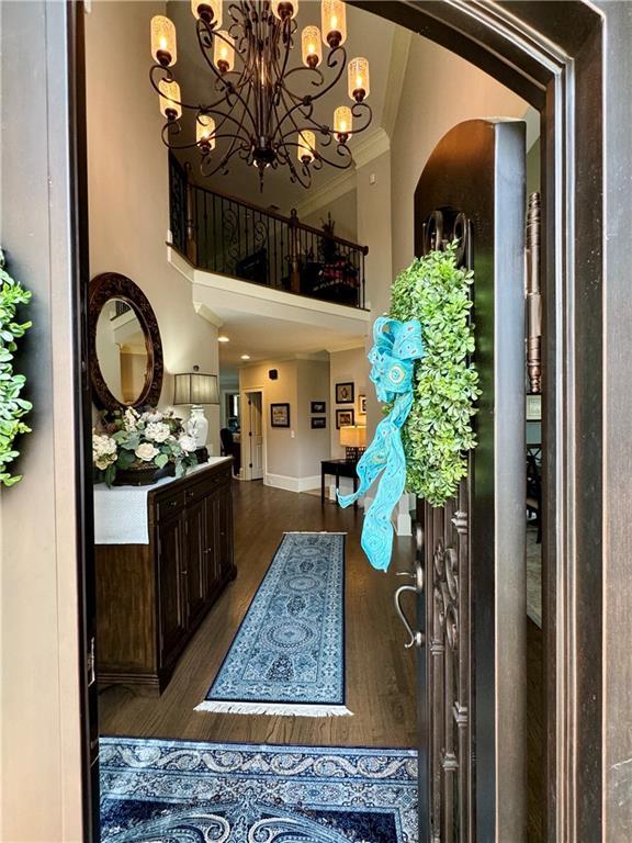 foyer with crown molding, dark wood finished floors, a towering ceiling, and an inviting chandelier