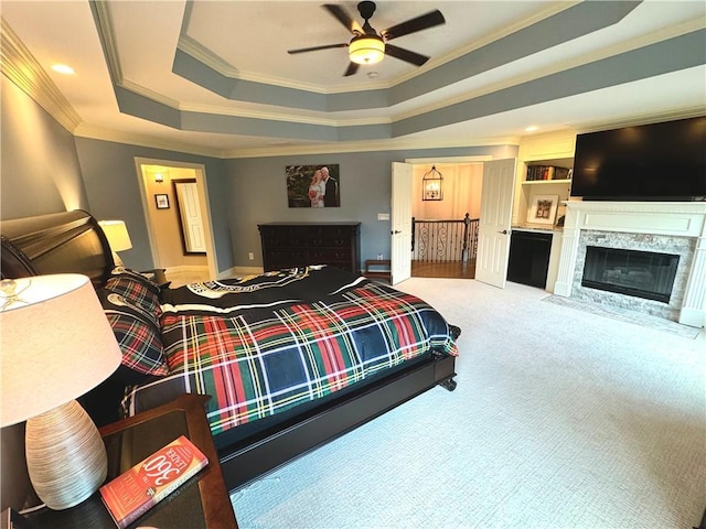 carpeted bedroom with ceiling fan, a fireplace with flush hearth, baseboards, a tray ceiling, and crown molding