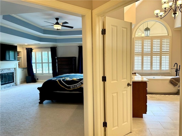 bedroom featuring a tray ceiling, a notable chandelier, light colored carpet, ornamental molding, and a stone fireplace