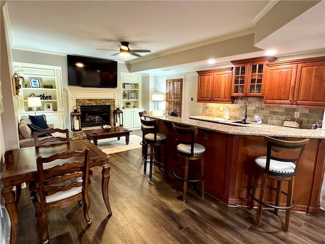 bar with crown molding, dark wood finished floors, a ceiling fan, and a stone fireplace