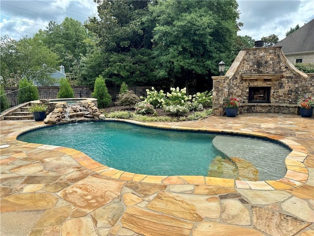 view of swimming pool with an outdoor stone fireplace, a patio area, a fenced backyard, and a fenced in pool