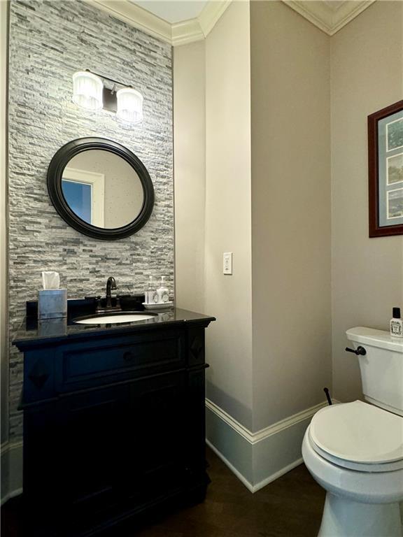 bathroom with toilet, wood finished floors, vanity, baseboards, and crown molding