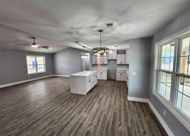 kitchen featuring pendant lighting, dark wood-type flooring, a center island, a textured ceiling, and white cabinets