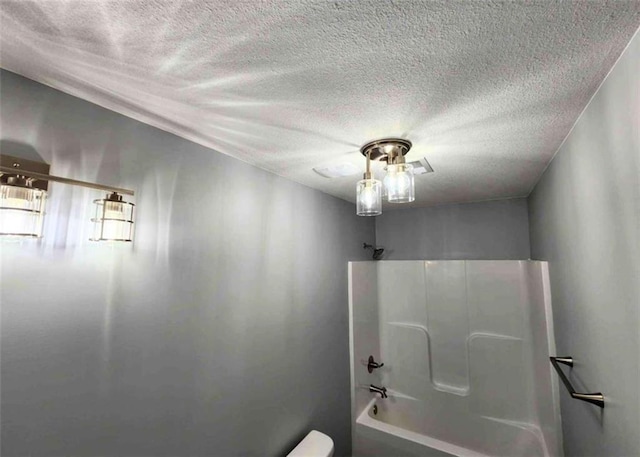 bathroom with washtub / shower combination, toilet, and a textured ceiling