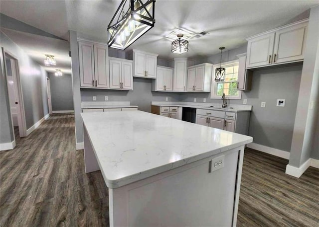 kitchen with pendant lighting, dark wood-type flooring, a center island, light stone countertops, and white cabinets