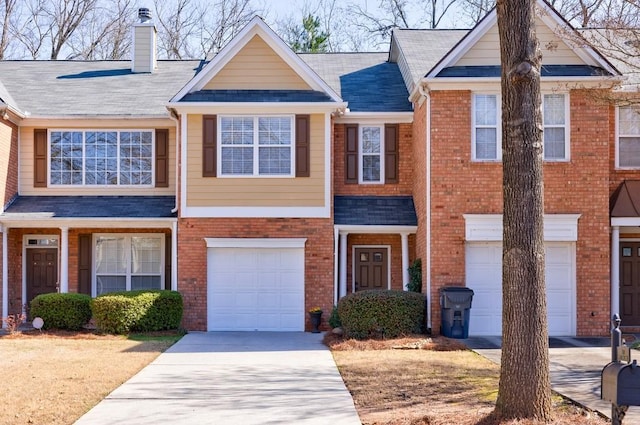 view of property featuring driveway, brick siding, a chimney, and an attached garage