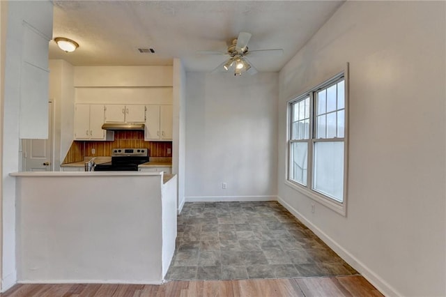 kitchen with baseboards, visible vents, a peninsula, stainless steel range with electric cooktop, and under cabinet range hood