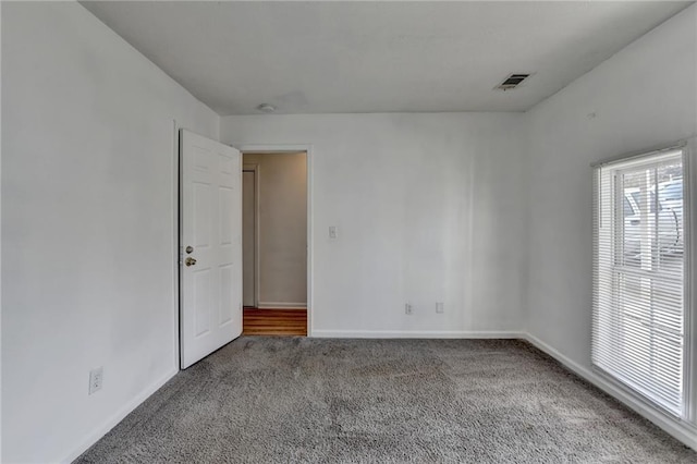 empty room with carpet, visible vents, and baseboards