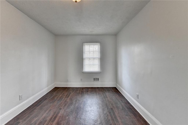 spare room featuring visible vents, dark wood finished floors, and baseboards