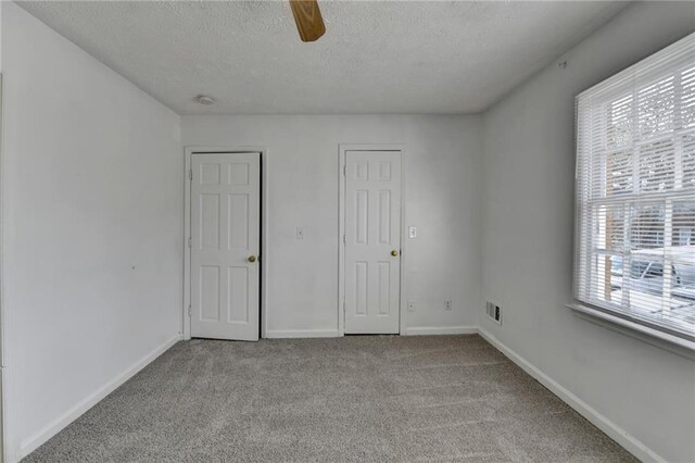 unfurnished bedroom featuring a textured ceiling, light carpet, visible vents, a ceiling fan, and baseboards