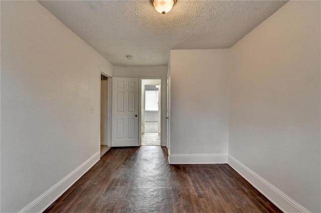 unfurnished room with dark wood-style flooring, a textured ceiling, and baseboards