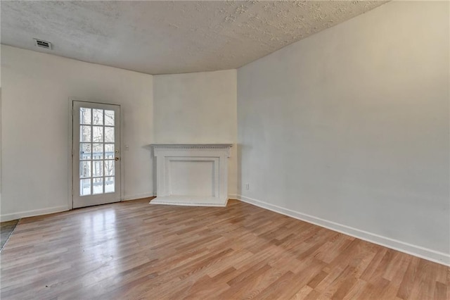 unfurnished living room with light wood finished floors, baseboards, visible vents, and a textured ceiling