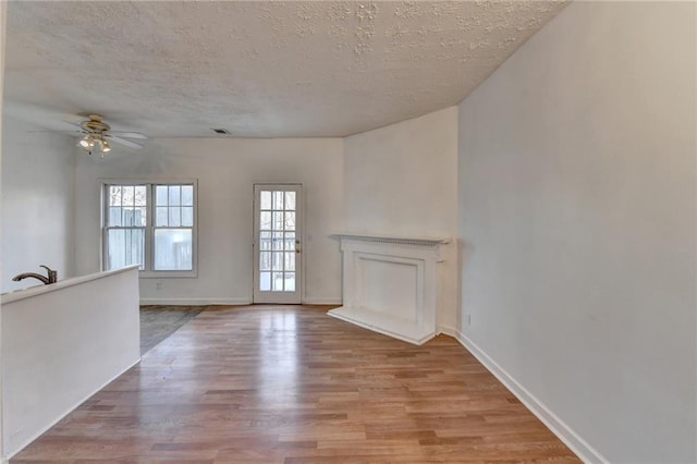 unfurnished living room featuring a ceiling fan, light wood-type flooring, a textured ceiling, and baseboards