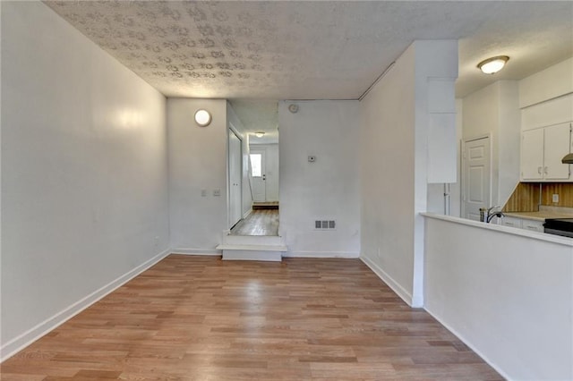 spare room featuring light wood-type flooring, visible vents, a sink, and baseboards