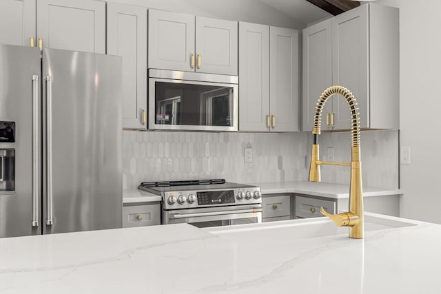 6564 Bermuda Ln, Flowery Branch, GA 30542 - kitchen featuring appliances with stainless steel finishes, decorative backsplash, light stone countertops, lofted ceiling, and gray cabinetry
