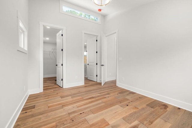 unfurnished bedroom with a walk in closet, recessed lighting, a closet, light wood-style flooring, and baseboards