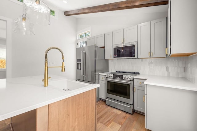 kitchen featuring tasteful backsplash, lofted ceiling with beams, appliances with stainless steel finishes, light wood-style floors, and a sink