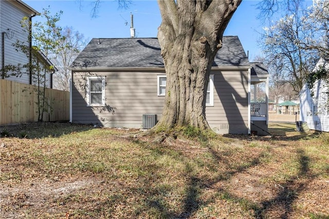 rear view of property featuring cooling unit, a shingled roof, fence, crawl space, and a lawn