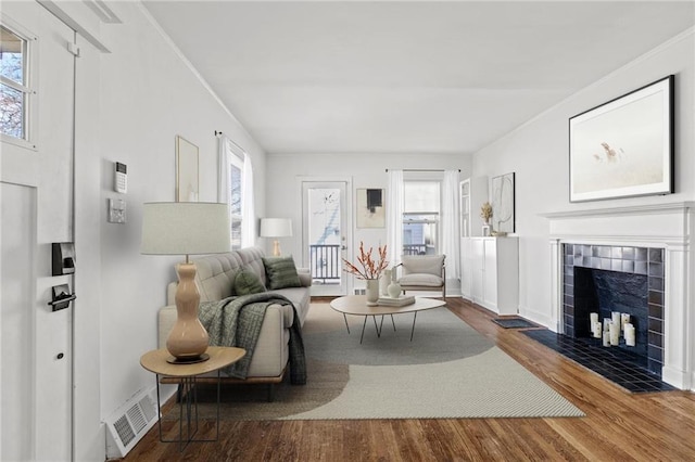 living room with plenty of natural light, visible vents, wood finished floors, and a tile fireplace