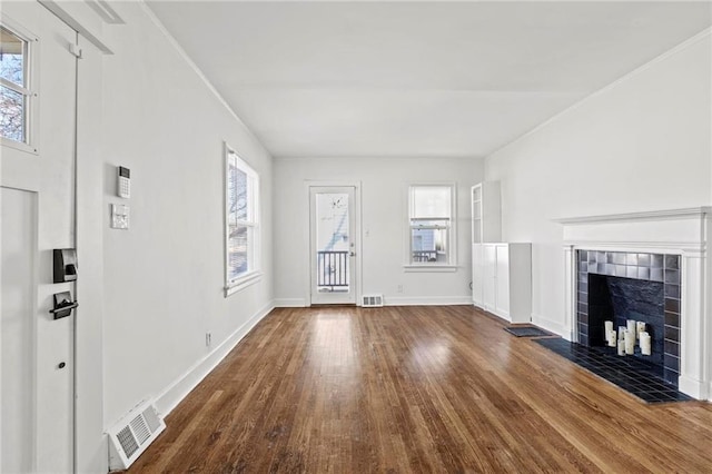 unfurnished living room with a wealth of natural light, wood finished floors, a tile fireplace, and visible vents