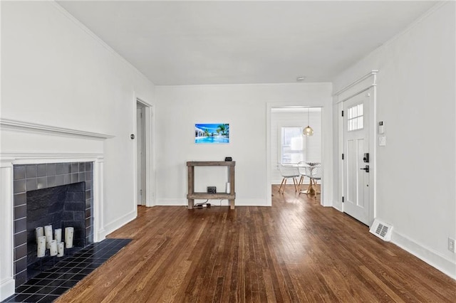 unfurnished living room with a tiled fireplace, wood finished floors, visible vents, and baseboards