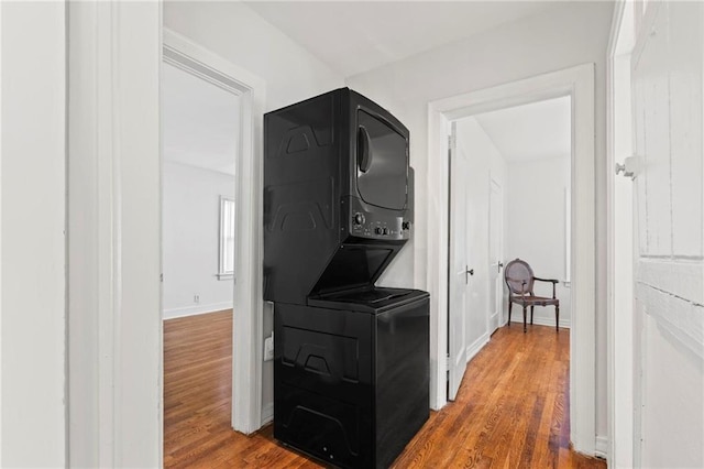 hallway with stacked washer / dryer, wood finished floors, and baseboards