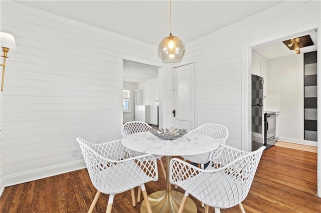 dining area featuring wooden walls, baseboards, and wood finished floors