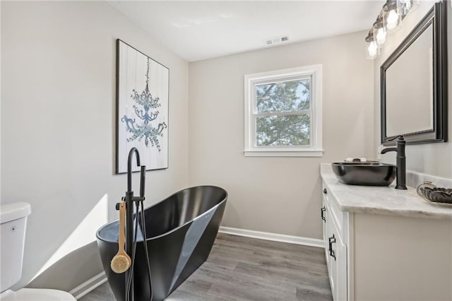 bathroom featuring hardwood / wood-style flooring, toilet, a tub to relax in, and vanity