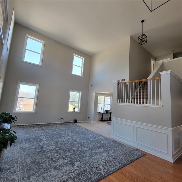 unfurnished living room featuring light wood-type flooring, a towering ceiling, and plenty of natural light