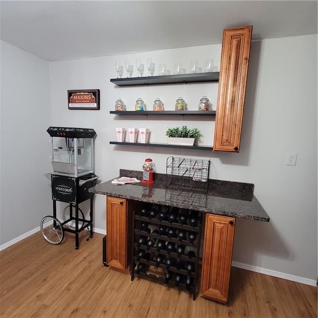 bar featuring light wood-type flooring and dark stone countertops