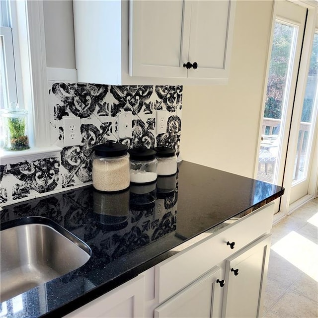 kitchen with dark stone countertops, white cabinetry, light tile patterned floors, and decorative backsplash