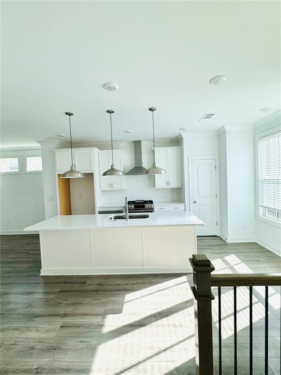 kitchen featuring an island with sink, white cabinetry, pendant lighting, wall chimney exhaust hood, and sink