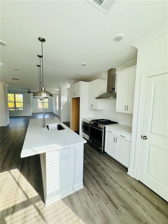 kitchen featuring visible vents, appliances with stainless steel finishes, white cabinetry, a sink, and wall chimney exhaust hood