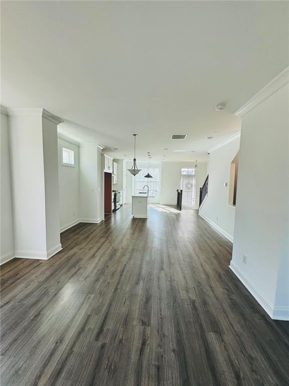 unfurnished living room with ornamental molding, dark wood finished floors, visible vents, and baseboards