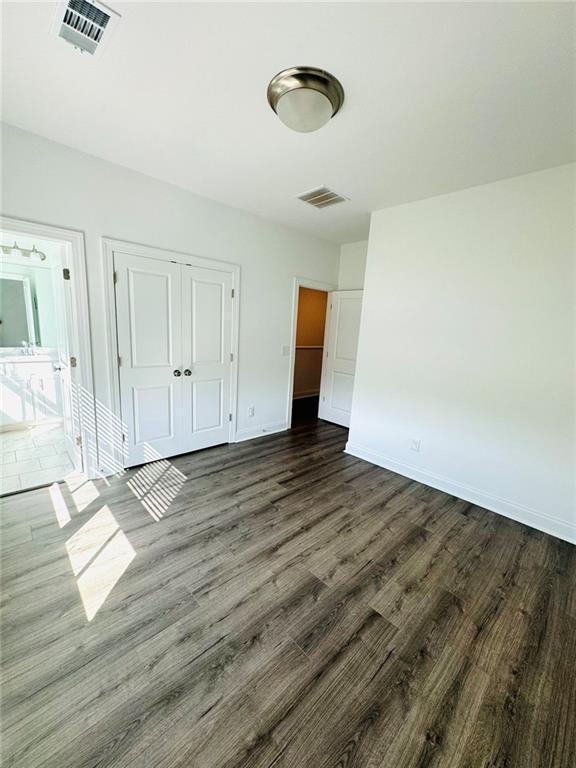 unfurnished bedroom with baseboards, visible vents, dark wood-type flooring, and a closet