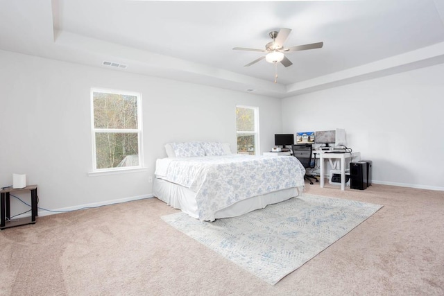 bedroom with light colored carpet, ceiling fan, and a tray ceiling