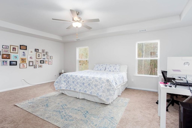 bedroom with a tray ceiling, multiple windows, ceiling fan, and light colored carpet